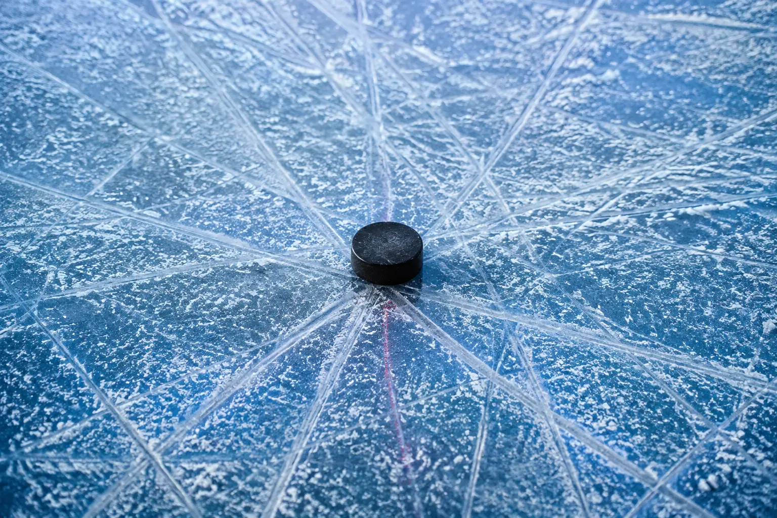 Skate grooves converging on a single black puck on blue ice